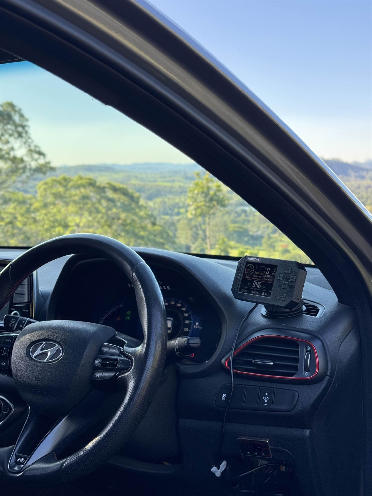 An Anvil prototype on a dash mount beside the steering wheel, a green valley through the windscreen
