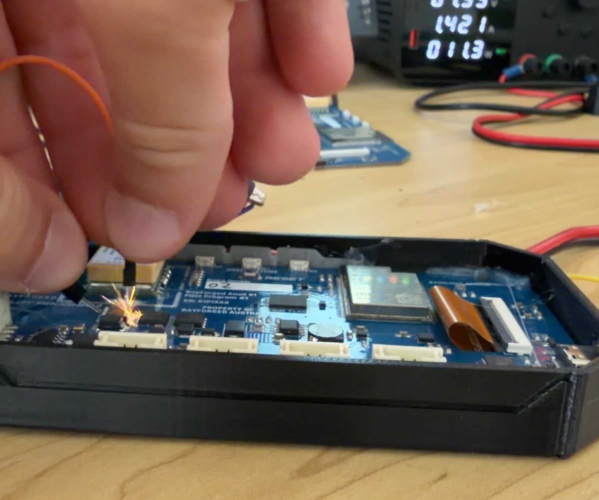 A hand holding a wire to a prototype circuit board in its case, a spark where it shorts